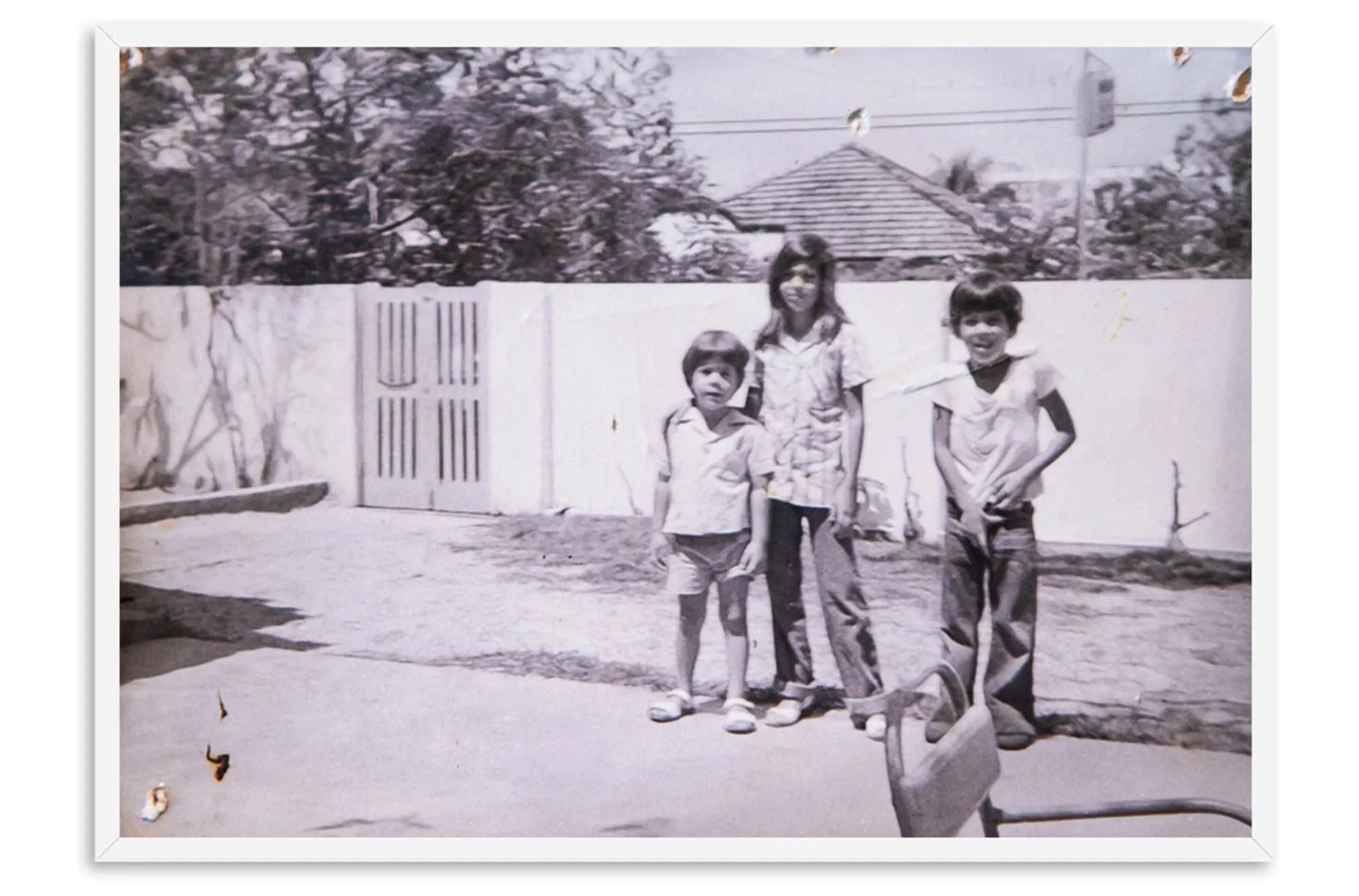 Foto antiga, em preto e branco, de três irmãos na frente de casa