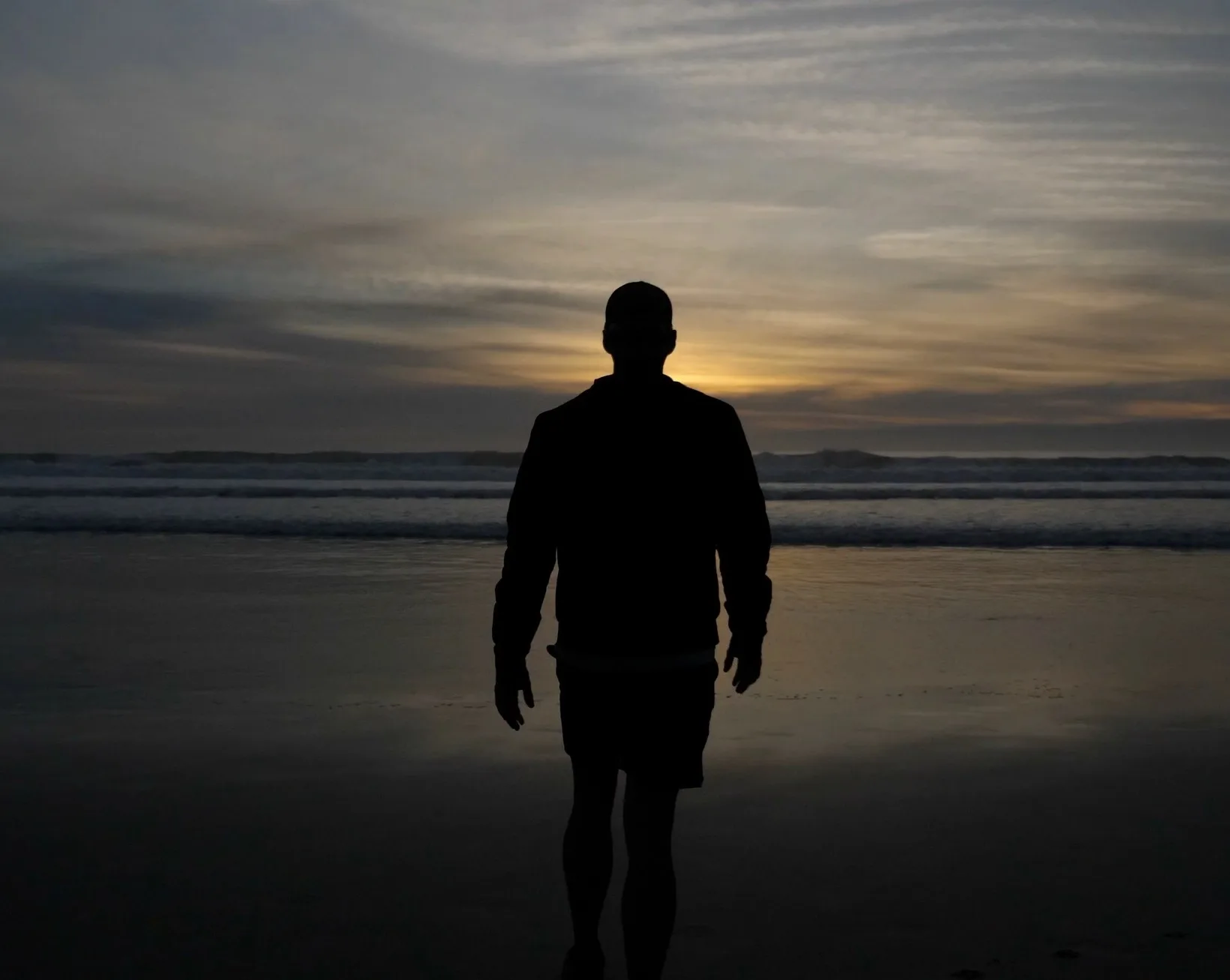 Homem caminhando na praia ao entardecer, em silhueta